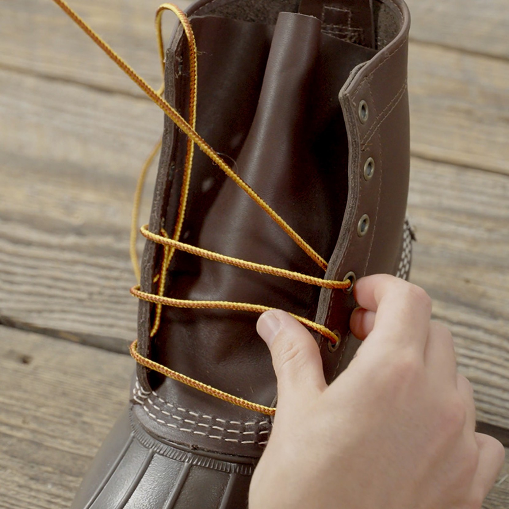 Hand threading yellow lace through eyelet on a brown leather boot. 