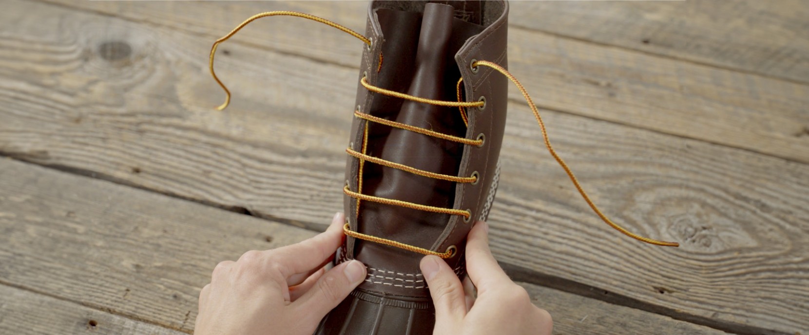 Brown boot with yellow laces fully threaded, hands holding the boot. 
