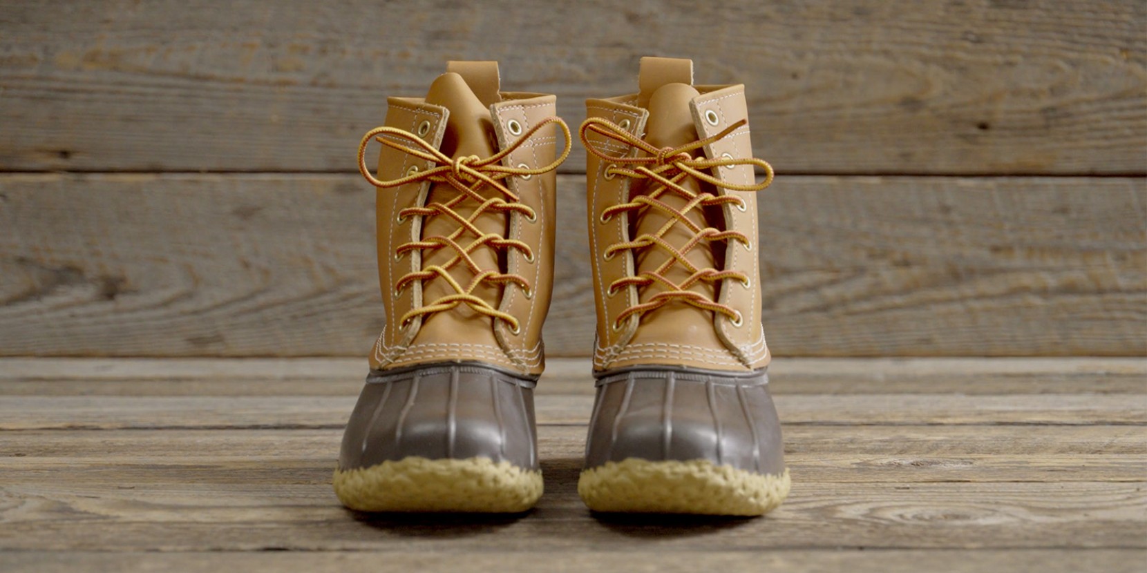 Pair of tan leather boots with yellow laces side by side on a wooden surface.