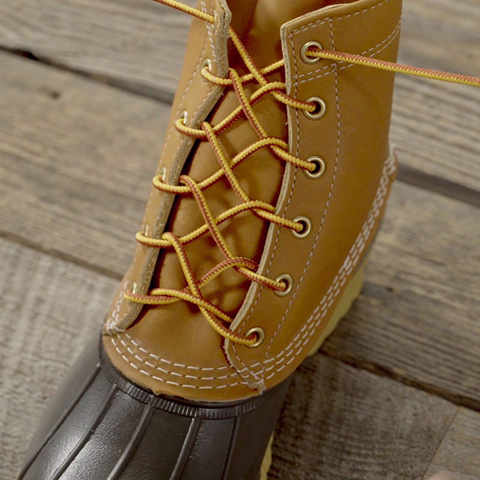Tan leather boot with yellow laces, open and resting on a wooden surface. 