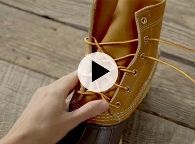 Hand adjusts the laces of the L L Bean Boot; play button icon appears over image.