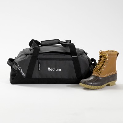 Medium gray L L Bean duffle bag with black straps, displayed beside a tan Bean Boot.