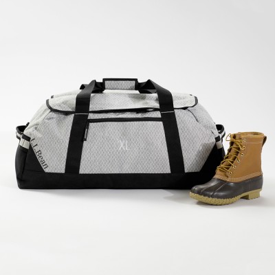 Extra-large gray patterned L L Bean duffle bag with black straps, next to a tan Bean Boot.