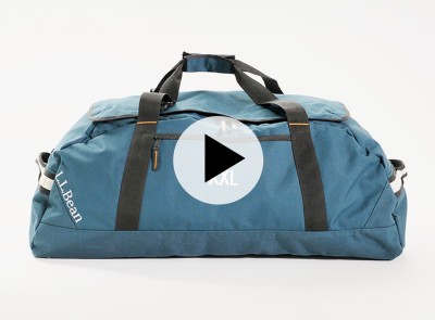 Blue duffle bag with black straps and XXL embroidered, shown on a white background; play button icon over image.
