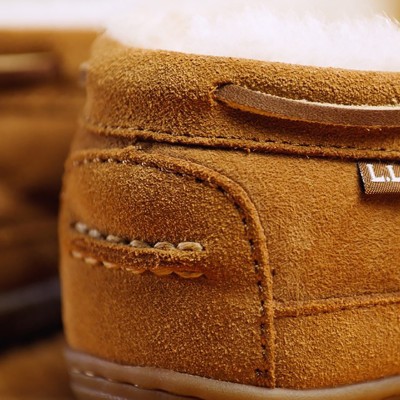 Close-up of the back of a tan suede moccasin slipper with stitched detailing, fleece lining, and L L Bean tag.