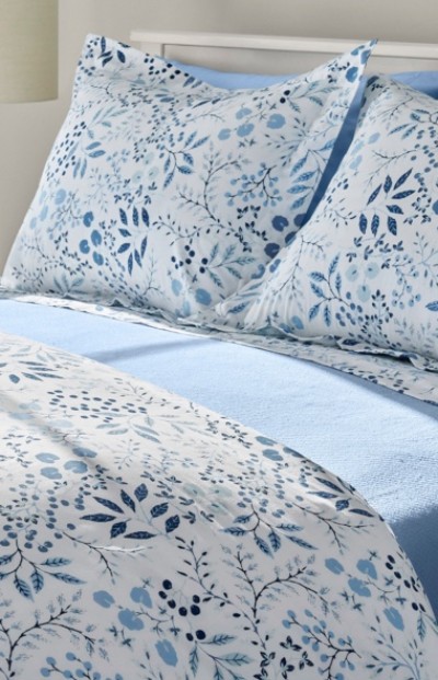 A neatly folded bed with blue and white floral sheets and pillows.