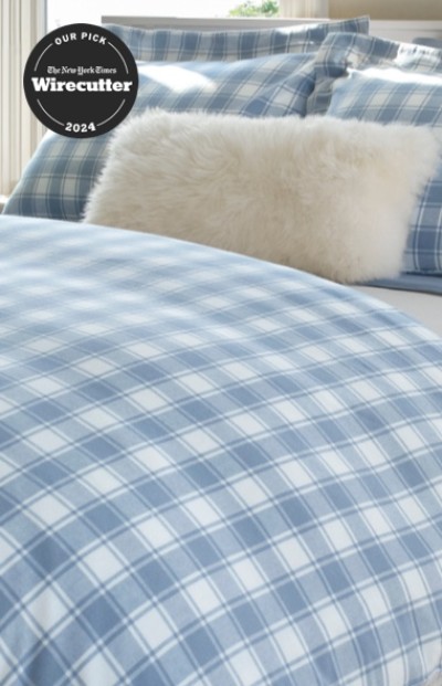 A neatly folded bed with blue and white plaid bedding and a New York Times wirecutter logo.