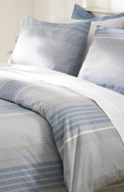 A neatly folded bed with matching blue and white bedding and pillows.