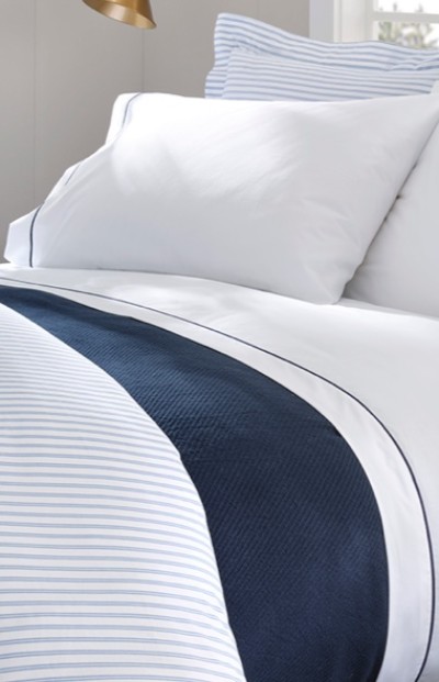 A neatly folded bed with white and blue striped bedding and pillows.