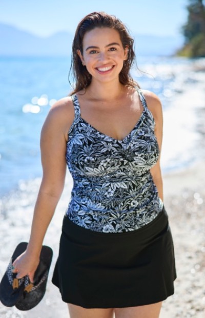 A woman walks a beach wearing a floral swim top and black skort.