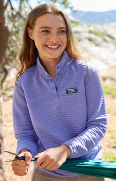 A woman in a purple long-sleeve shirt is holding a green hammock strap outdoors.