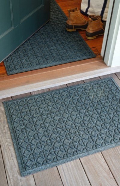 Two blue patterned doormats, one inside and one outside a door, with a pair of brown boots placed near the door.