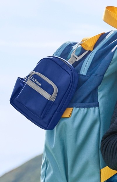 A blue and teal backpack with a small attached blue pouch labeled "L.L.Bean" is shown against a blurred outdoor background.