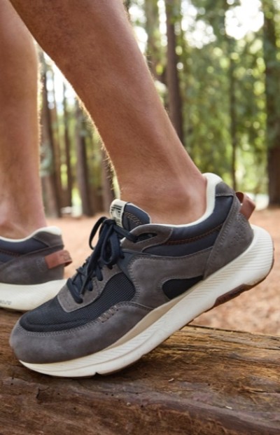 Close up of a person wearing gray and black sneakers, standing on a log in a forest.