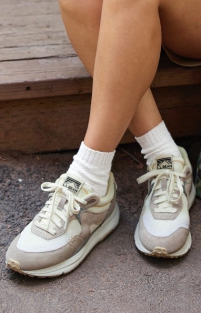 A woman wearing white socks and beige sneakers with the L L Bean logo sits on a wooden step.