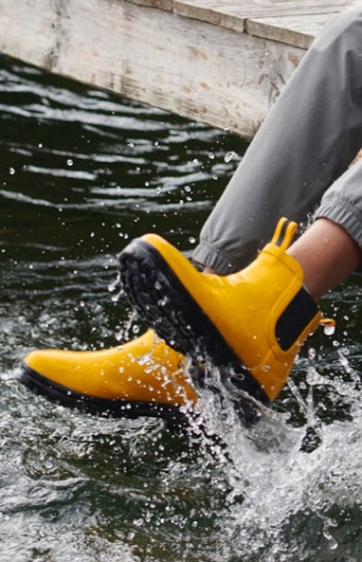 A child wearing yellow rain boots splashes water while sitting on a wooden dock.
