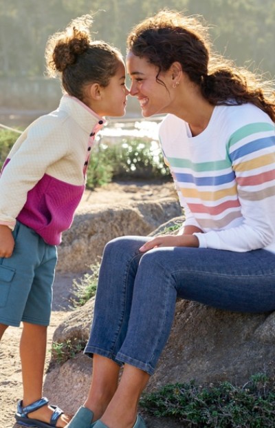 A child leans in to kiss an adult sitting on a rock outdoors.