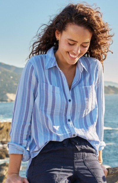 Woman with curly hair wearing a blue and white striped shirt, standing outdoors near a body of water.