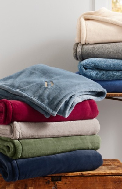 A stack of folded blankets in various colors, including blue, red, beige, green, and navy, placed on a wooden surface.