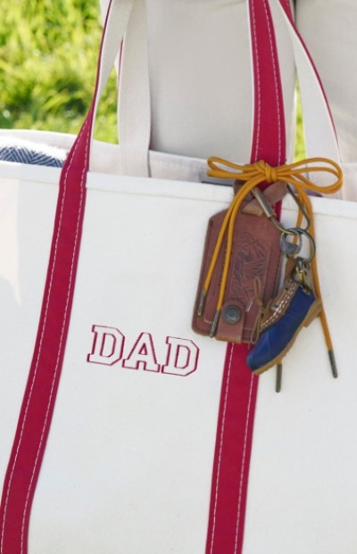 Close up image of a tote bag with red handles and a monogram sewn on the front with a gift tag.
