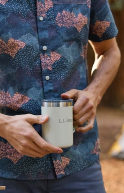 Close up image of a man in a short sleeve shirt holding a travel mug outside.