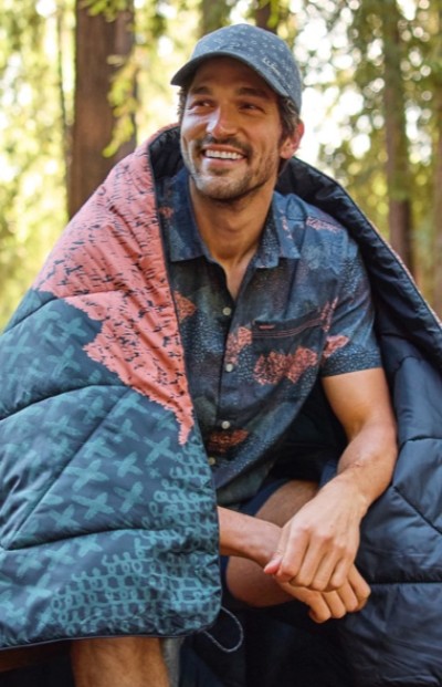 Smiling man in the forest wrapped in an outdoor blanket.