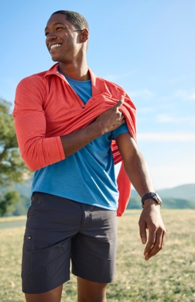 Smiling man putting on a long sleeve shirt and wearing shorts outside enjoying nature.