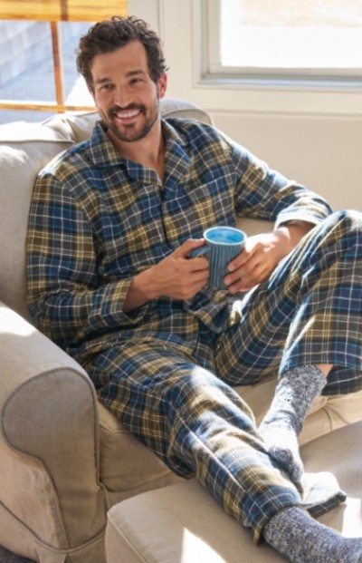 Smiling man lounging in pajamas while drinking coffee.