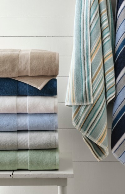 Stack of colorful folded towels on white table; two striped towels hang on the right against a white wooden wall.