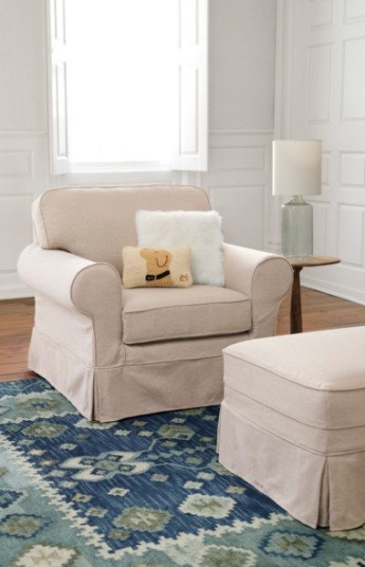 Beige armchair with pillows, matching ottoman, blue patterened rug, and side table with lamp in a bright room.