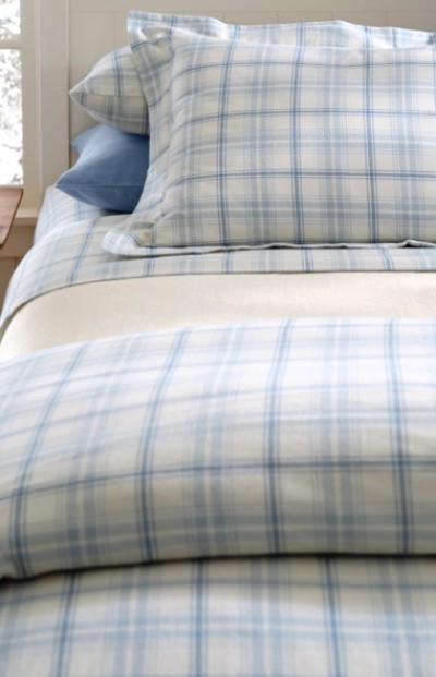Neatly made bed with blue and white plaid bedding, matching pillowcases, and a light blue accent pillow.