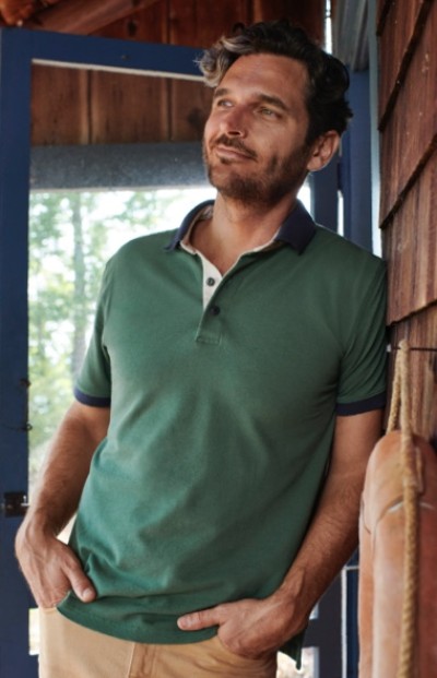 Waist up shot of man wearing a green polo leaning on an exterior cabin door.