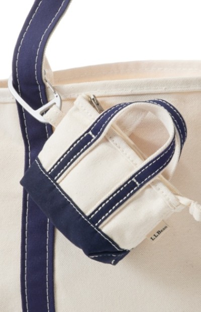 Close up image of a white micro tote with blue straps clipped to the handle of a larger white tote with blue straps.