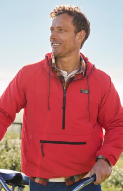 A man wearing a red jacket with front zipper pocket holds bicycle handlebars outdoors.