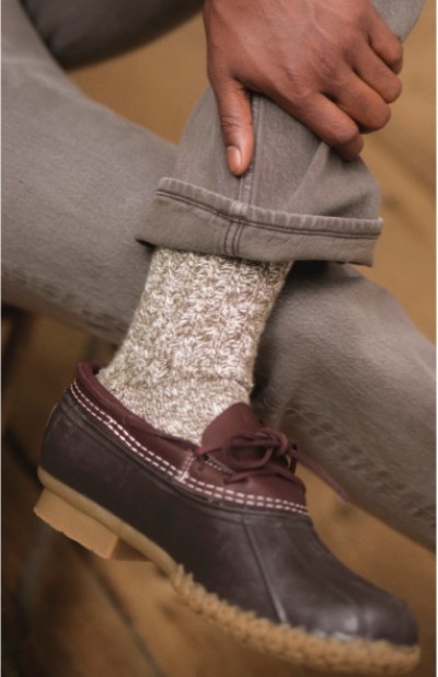 Close up of a person sitting with legs crossed wearing gray pants, gray wool socks, and brown L. L. Bean rubber mocs.