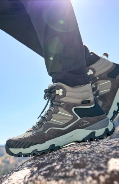 Close-up of gray and light teal hiking boots on a rock, with sunlight and a clear blue sky in the background.