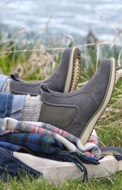 Close up of a person wearing gray boots and jeans laying on a blanket, surrounded by grass and plants.