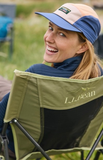 Person in red beanie and blue jacket carries green backpack with trekking poles, map, and gear attached.