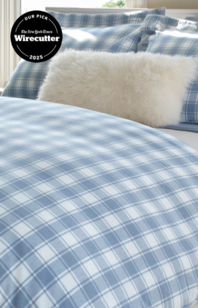 A neatly folded bed with blue and white plaid bedding and a New York Times wirecutter logo.