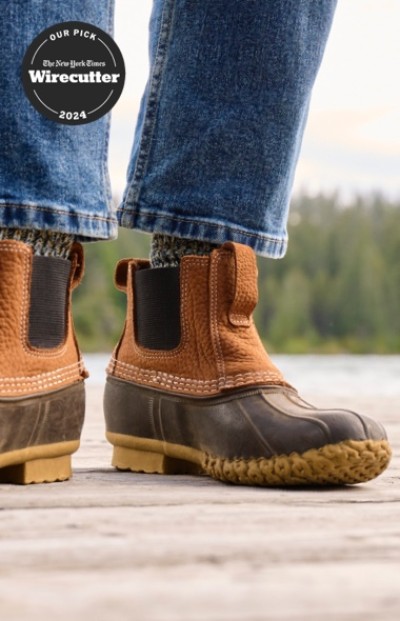 Close up of a person in brown L. L. Bean Chelsea boots and jeans standing on a wooden dock and a Wirecutter top pick badge.
