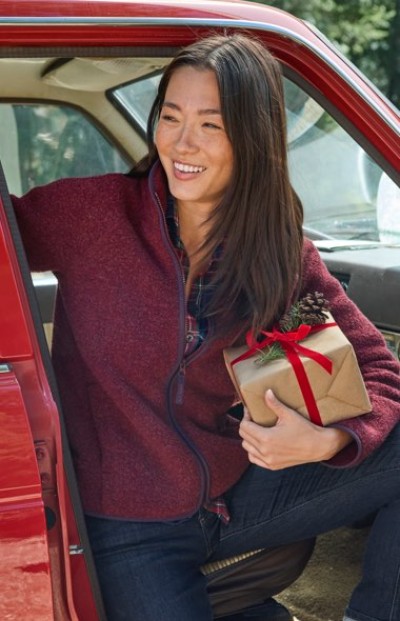 Person in red jacket holding a gift box with red ribbon, stepping out of a red car.