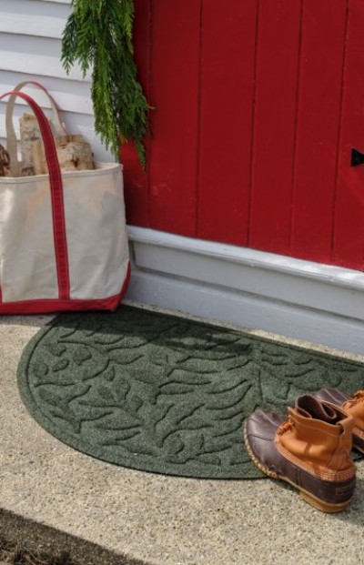 Green doormat, brown boots, and a white tote with red trim placed outside a red door in a welcoming outdoor scene.