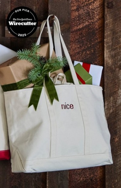 White tote bag with “nice” embroidered, filled with wrapped gifts and greenery, set against a rustic wooden background.