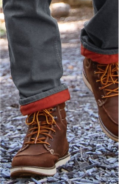 Person in brown boots with yellow laces and red-cuffed pants walking on a gravel path.