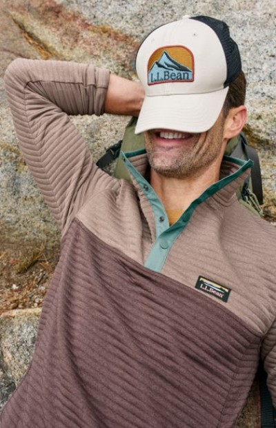 Person in light and dark brown colorblock pullover wearing an L. L. Bean trucker hat pulled low over their face.