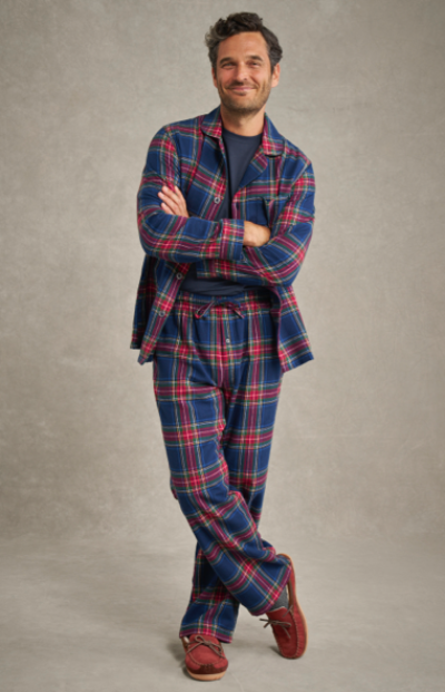 A person in a blue and red plaid flannel pajama set and red moccasin-style slippers stands in front of a plain background.
