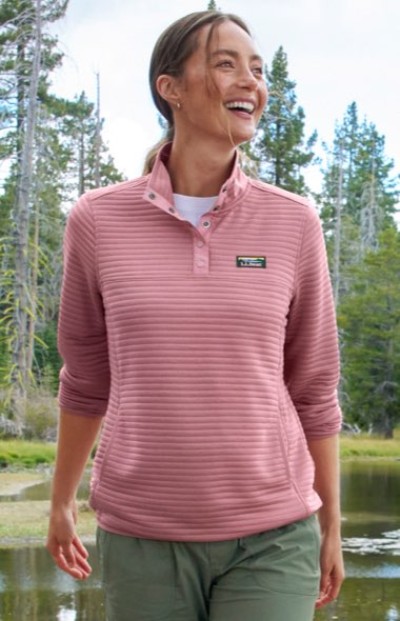 A woman wearing a pink L. L. Bean pullover and green pants while walking outdoors.