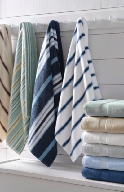 Stack of colorful folded towels on a white table; four striped towels hang on the left against a white wooden wall.