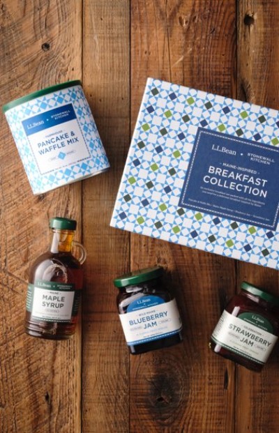 Breakfast gift set displayed on a wooden surface includes pancake mix, maple syrup, blueberry jam, and strawberry jam.