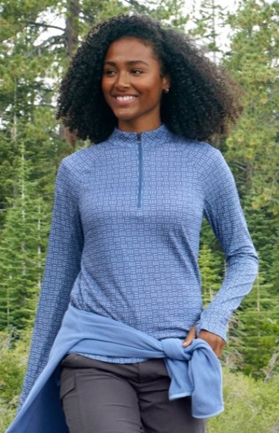 Person in a blue patterned long-sleeve zip-neck top with a sweatshirt tied at the waist, paired with dark outdoor pants.